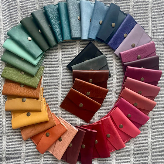 Circular arrangement of Mini Envelope Wallets in various colors on a textured surface.