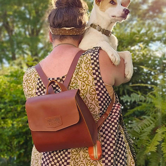 Person with a brown archived PLG backpack holding a dog outdoors