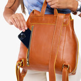 Sienna | Model holding a leather backpack pulling a black smartphone out of the back zipper pocket