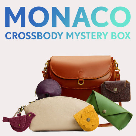 Monaco Crossbody in Madrone next to Mockingbird Pouch, Eclipse Makeup Bag, Fortune Cookie Keychain, Petunia Pouch, Sunglasses Case, and Lovebug Wallet. Text reads "Monaco Crossbody Mystery Box" 