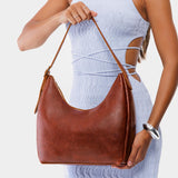 Nutmeg Medium | Model holding u-shaped, flat-bottomed leather shoulder bag with adjustable strap