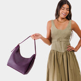 Plum Medium | Model holding u-shaped, flat-bottomed leather shoulder bag with adjustable strap
