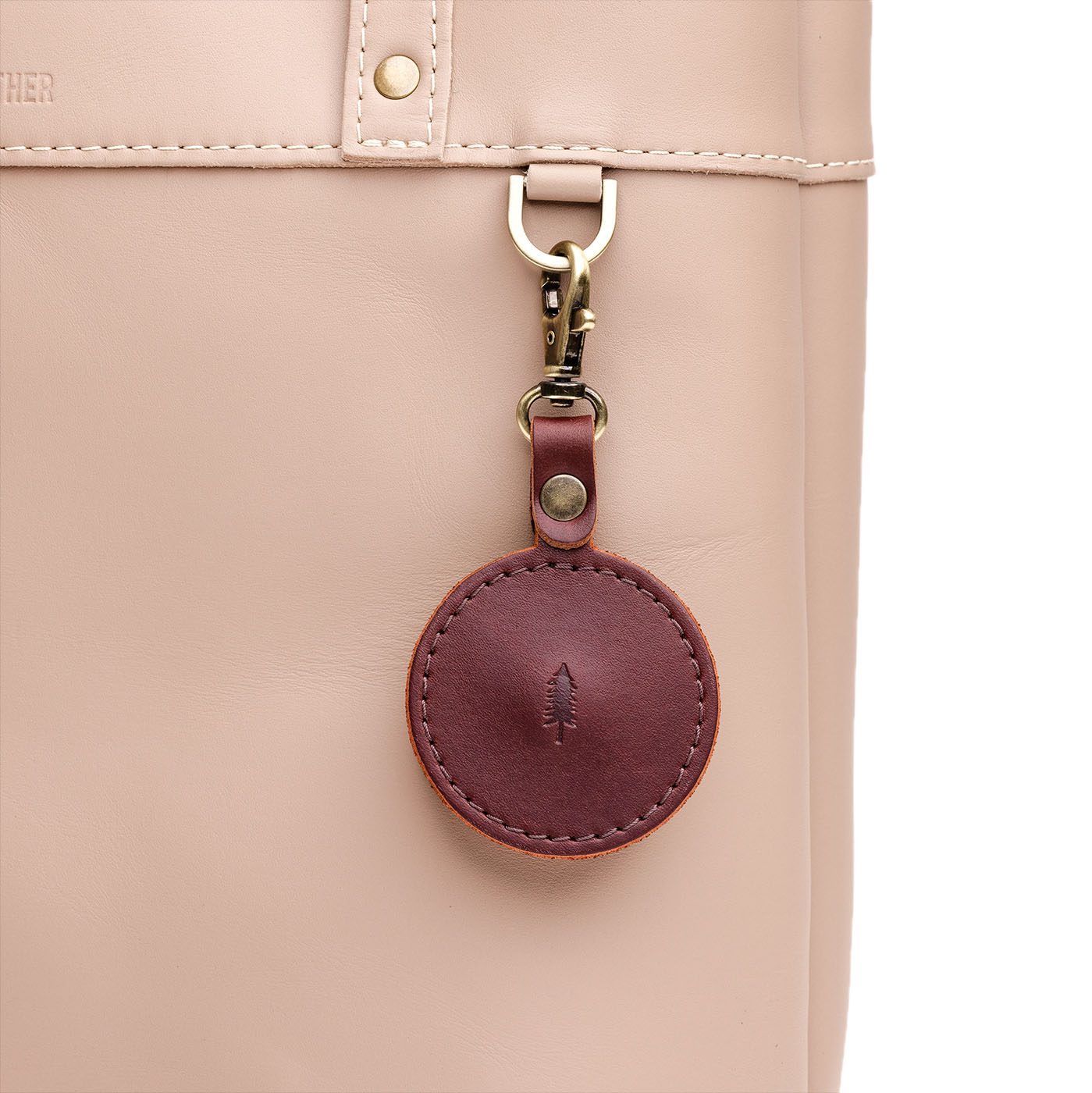 Cognac | Circle-shaped airtag holder keychain with a swivel lobster clasp on bag