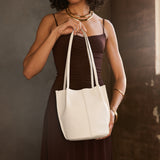 Bone Classic | Model holding sleeveless dark brown dress carrying petite bucket shaped tote bag with matching leather handles against dark grey background