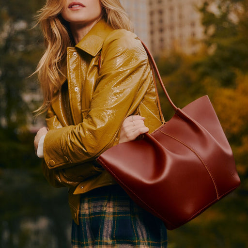 A model wearing a glossy mustard yellow jacket and carrying a large leather tote bag over shoulder featured image