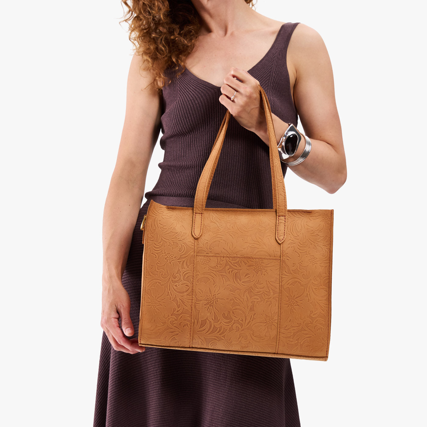 Desert Flower | Model holding structured wide embossed leather tote bag with overlapping panels and crossbody strap