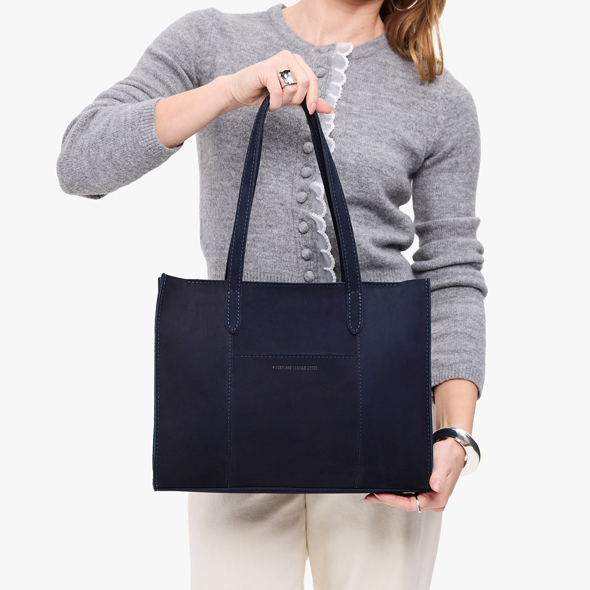 Velvet Blue*East/West | Model holding structured wide tote bag with overlapping panels and crossbody strap