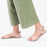 Crema | Close-up of a person wearing light green cropped pants and cream flat sandals with an ankle strap and buckle, shown against a plain background.