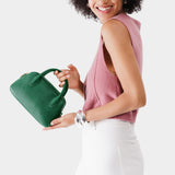 Bacalar Small | A bowler styled bag with a crossbody strap being held by a model wearing a pink knit vest