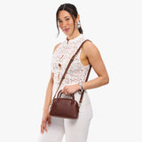 Cognac Small | A bowler styled bag with a crossbody strap being worn by a model in a white outfit