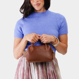 Nutmeg Small | A Bowler style purse with a crossbody strap being held by a model