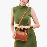 Sienna Small | A bowler styled bag with a crossbody strap being held by a model wearing a dress