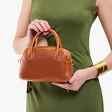 Sienna Small | A bowler styled bag with a crossbody strap being held by a model wearing a dress