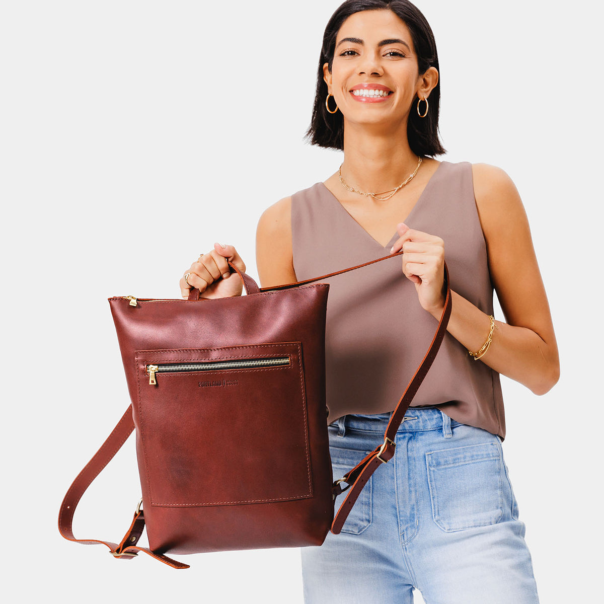 All Color: Cognac | Model holding rectangular slim leather backpack