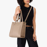 Stone North/South | Model holding structured wide tote bag with overlapping panels and crossbody strap