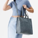 Storm North/South | Model holding structured large tote bag with overlapping panels and crossbody strap