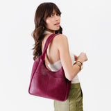 Orchid Large | A model holding a u-shaped, flat-bottomed leather shoulder bag with two outside pockets