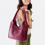 Orchid Large | A model holding a u-shaped, flat-bottomed leather shoulder bag with two outside pockets