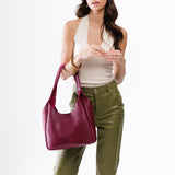 Orchid Large | A model holding a u-shaped, flat-bottomed leather shoulder bag with two outside pockets