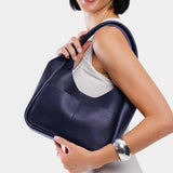Cobalt Medium | A model holding a u-shaped, flat-bottomed leather shoulder bag with two outside pockets
