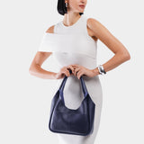 Cobalt Medium | A model holding a u-shaped, flat-bottomed leather shoulder bag with two outside pockets