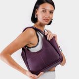 Plum Medium | A model holding a u-shaped, flat-bottomed leather shoulder bag with two outside pockets