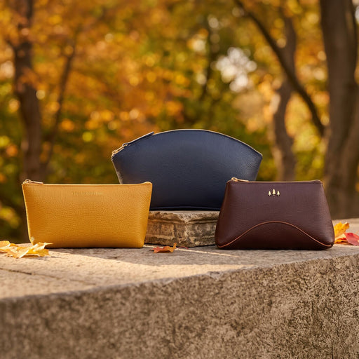 Three leather pouches are arranged on a stone ledge outdoors with a blurred autumn park background. featured image