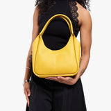 Pomello Medium | Model holding a u-shaped, flat-bottomed leather shoulder bag with two outside pockets