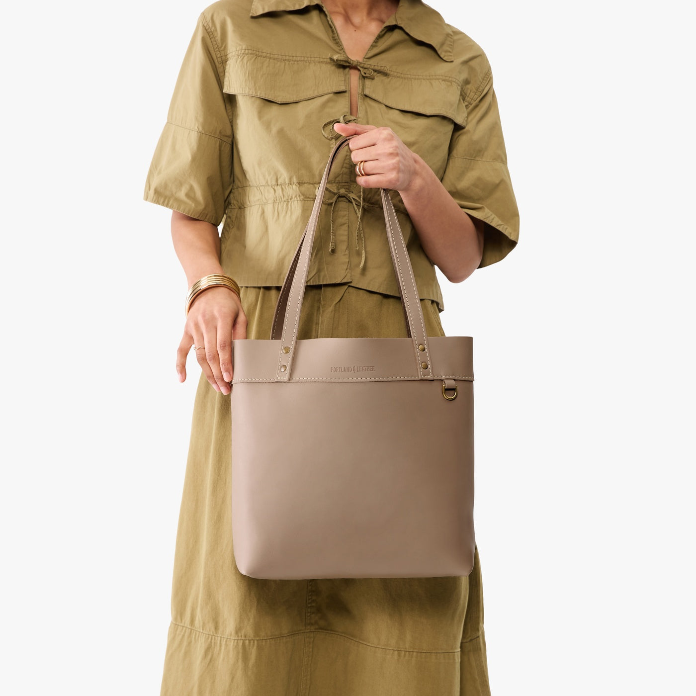 Stone*Medium*Classic | Model holding leather tote bag with riveted straps and exterior key loop 