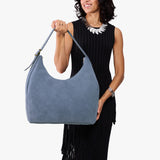 Denim Oversized | Model holding u-shaped, flat-bottomed leather shoulder bag with adjustable strap