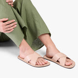 Crema | Close-up of model wearing light green pants and beige flat sandals, shown against a plain background