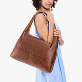 Asheville Large | A model holding a slouchy triangle shaped shoulder bag with a flap