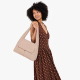 Taupe Medium | A model holding a slouchy triangle shaped shoulder bag with a flap